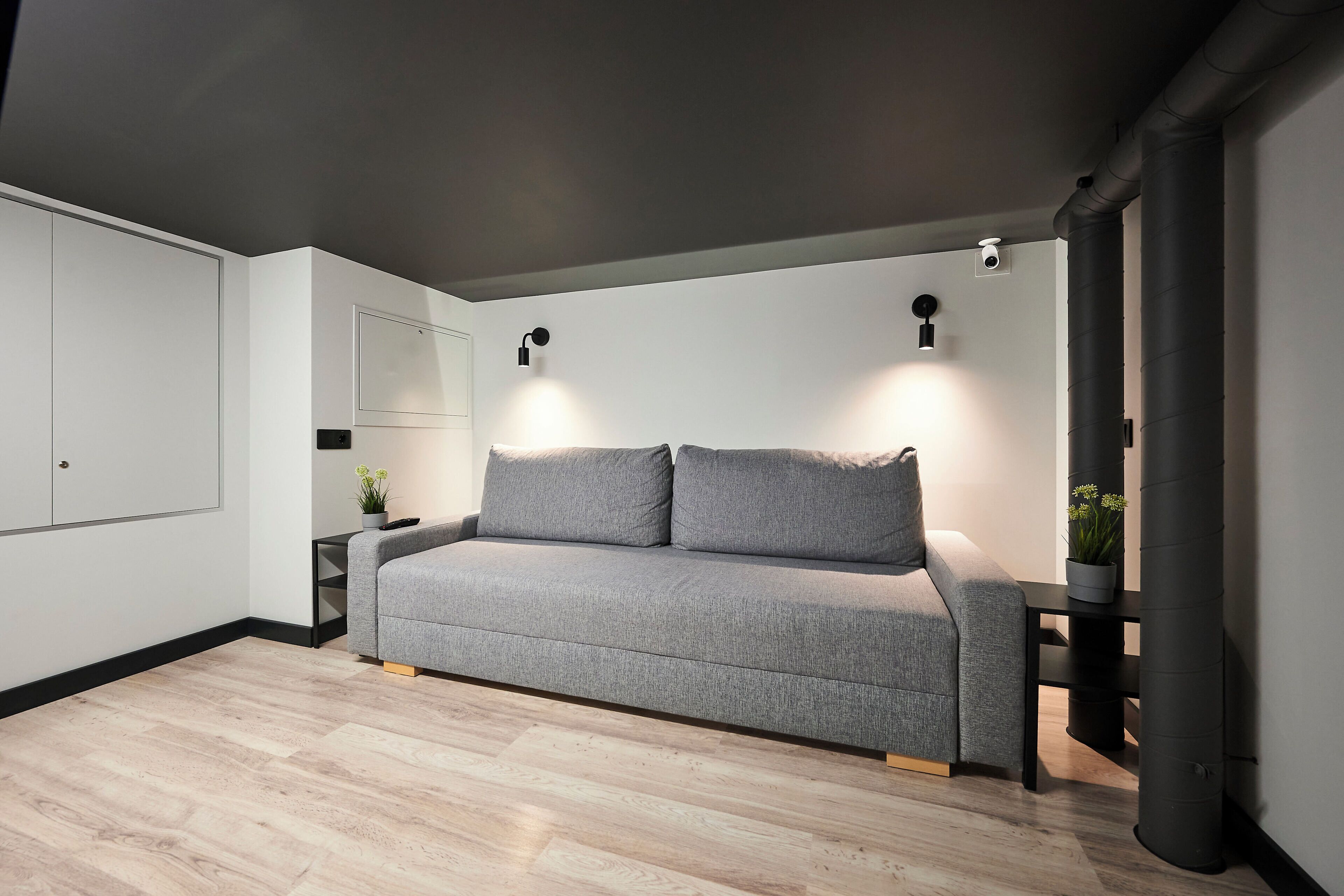 Una sala de estar moderna con un sofá gris, una mesita auxiliar con una planta y una lámpara de pared.