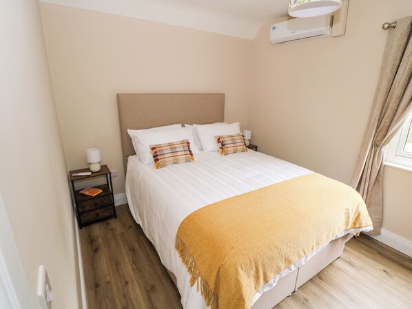 A bedroom with a bed, a bedside table, a lamp, and a window with curtains.