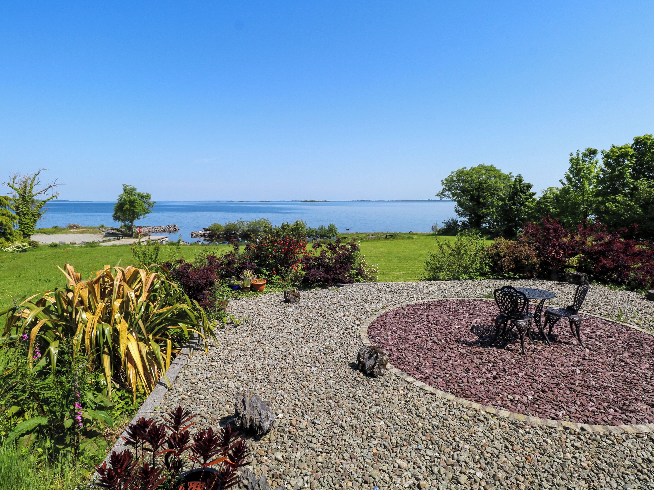 A garden with a circular seating area, a gravel path, and a view of the sea.