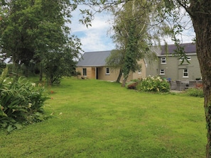 A residential property with a grassy yard, a wooden door, and a grey building with multiple windows.
