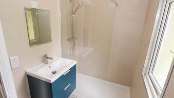 A bathroom with a glass shower enclosure, a white sink with a blue cabinet, and patterned floor tiles.