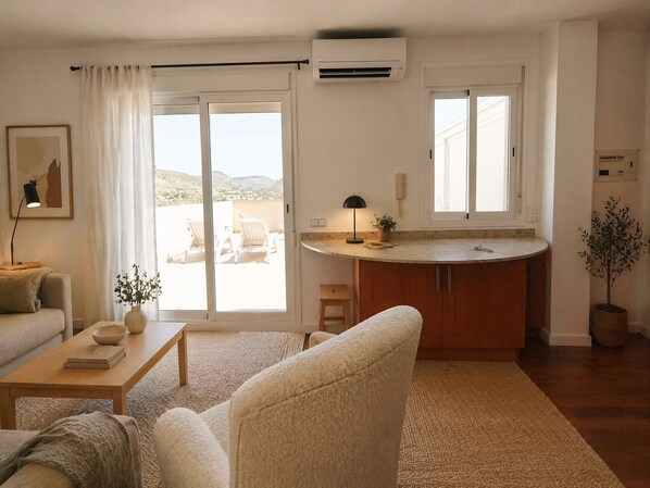 A living room with a sofa, a coffee table, a dining area with a table and chairs, and a kitchen with a countertop and cabinets.