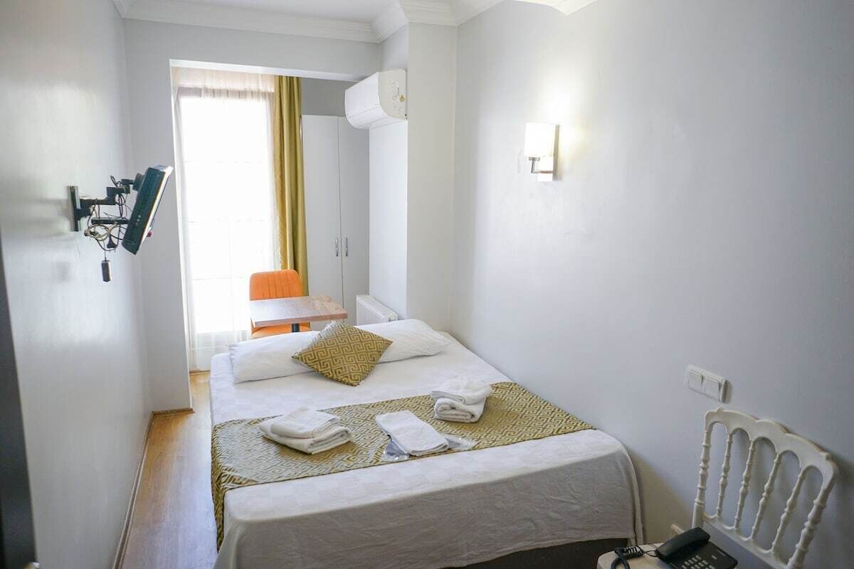 A hotel room with a bed, a desk, a chair, a radiator, and a wall-mounted phone.