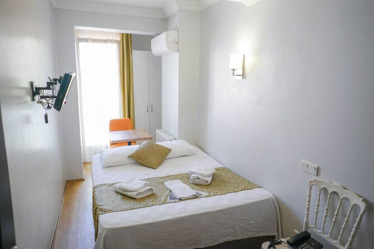 Ein Hotelzimmer mit Bett, Schreibtisch, Stuhl, Heizkörper und einem an der Wand befestigten Telefon.