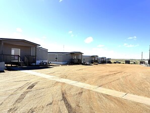 A row of mobile homes with picnic tables in front, a clear sky, and a dirt ground.