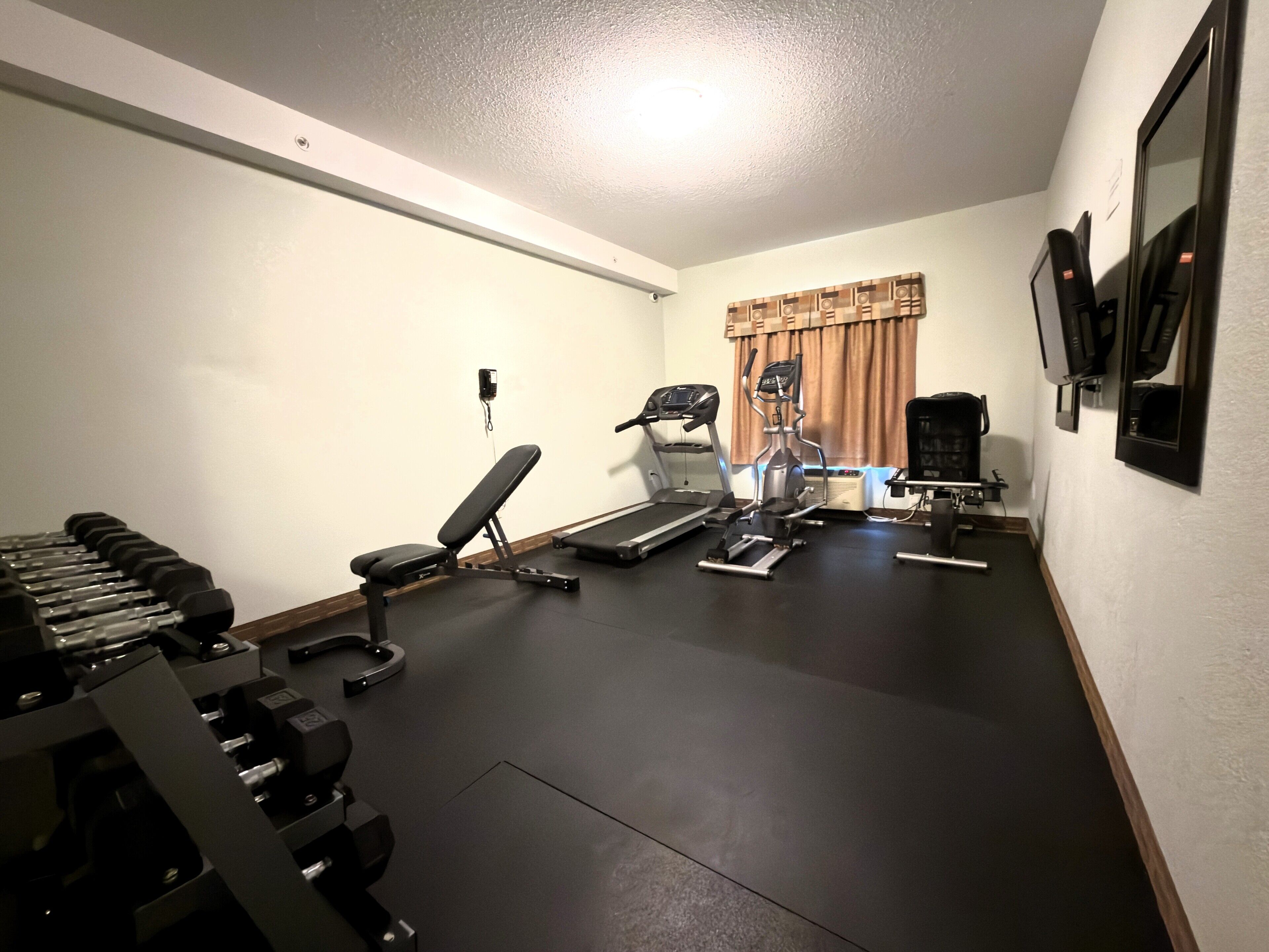 Una palestra in casa con attrezzature per esercizi, tra cui pesi, panca, tapis roulant ed ellittica.