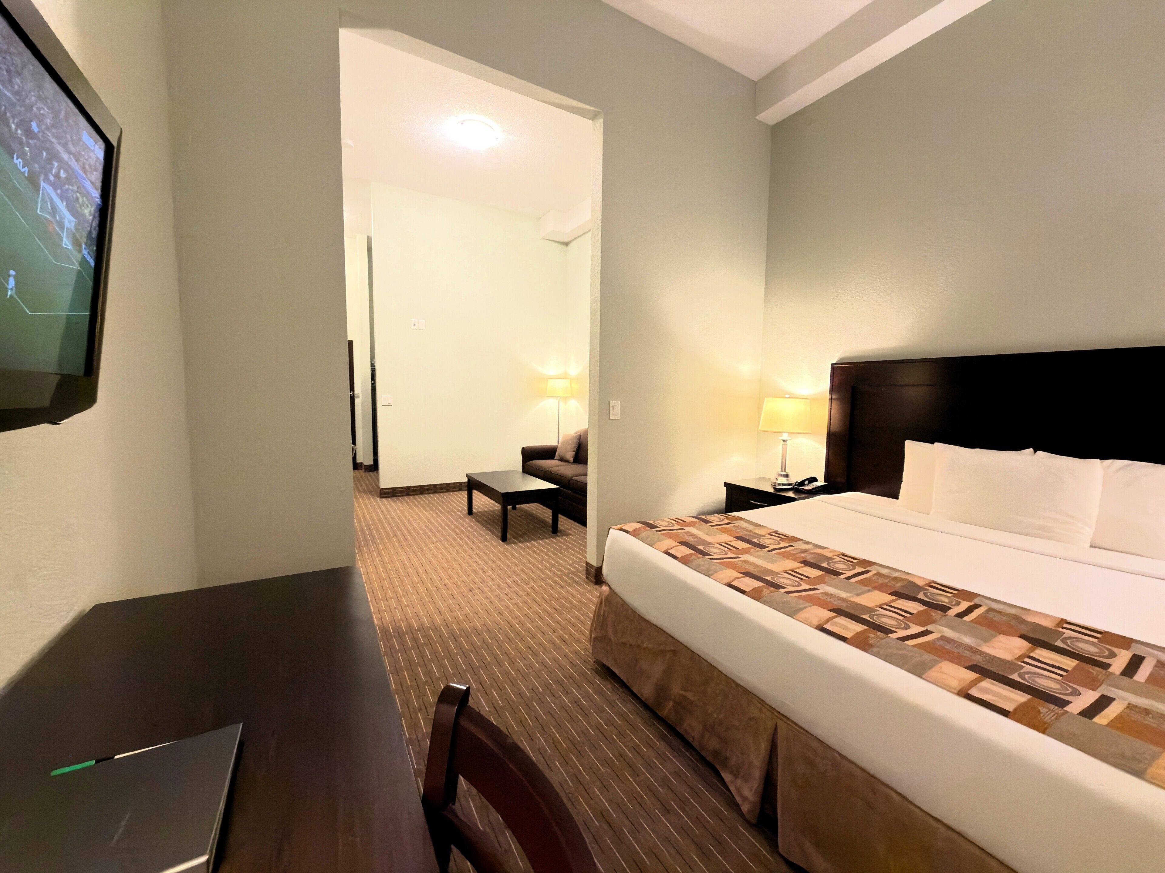 A hotel room with a bed, a desk, a chair, a TV, and a lamp.