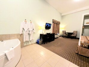 Habitación de hotel con bañera, escritorio con silla, televisor y cama.