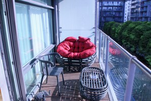 Ein Balkon mit einem Korbstuhl, einer rot gepolsterten Sitzgelegenheit und einem kleinen runden Tisch.