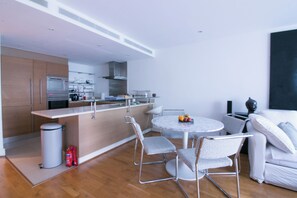 A modern kitchen with built-in appliances, a dining area with a round table and chairs, and a living area with a sofa and a sculpture. - Lux Modern 2BR Flat wth Balcony • Walk to Battersea Park, River, Mall, Transport (London)