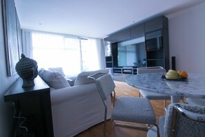 Ein modernes Wohnzimmer mit Sofa, Esstisch und Stühlen. Im Hintergrund ist eine Küchenzeile zu sehen.