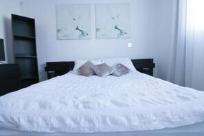 Ein Schlafzimmer mit einem großen Bett, zwei Nachttischen, einem Bücherregal und abstrakter Wandkunst.