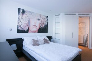 A modern bedroom with a large abstract painting, a neatly made bed, a bedside table, and a walk-in closet. - Lux Modern 2BR Flat wth Balcony • Walk to Battersea Park, River, Mall, Transport (London)