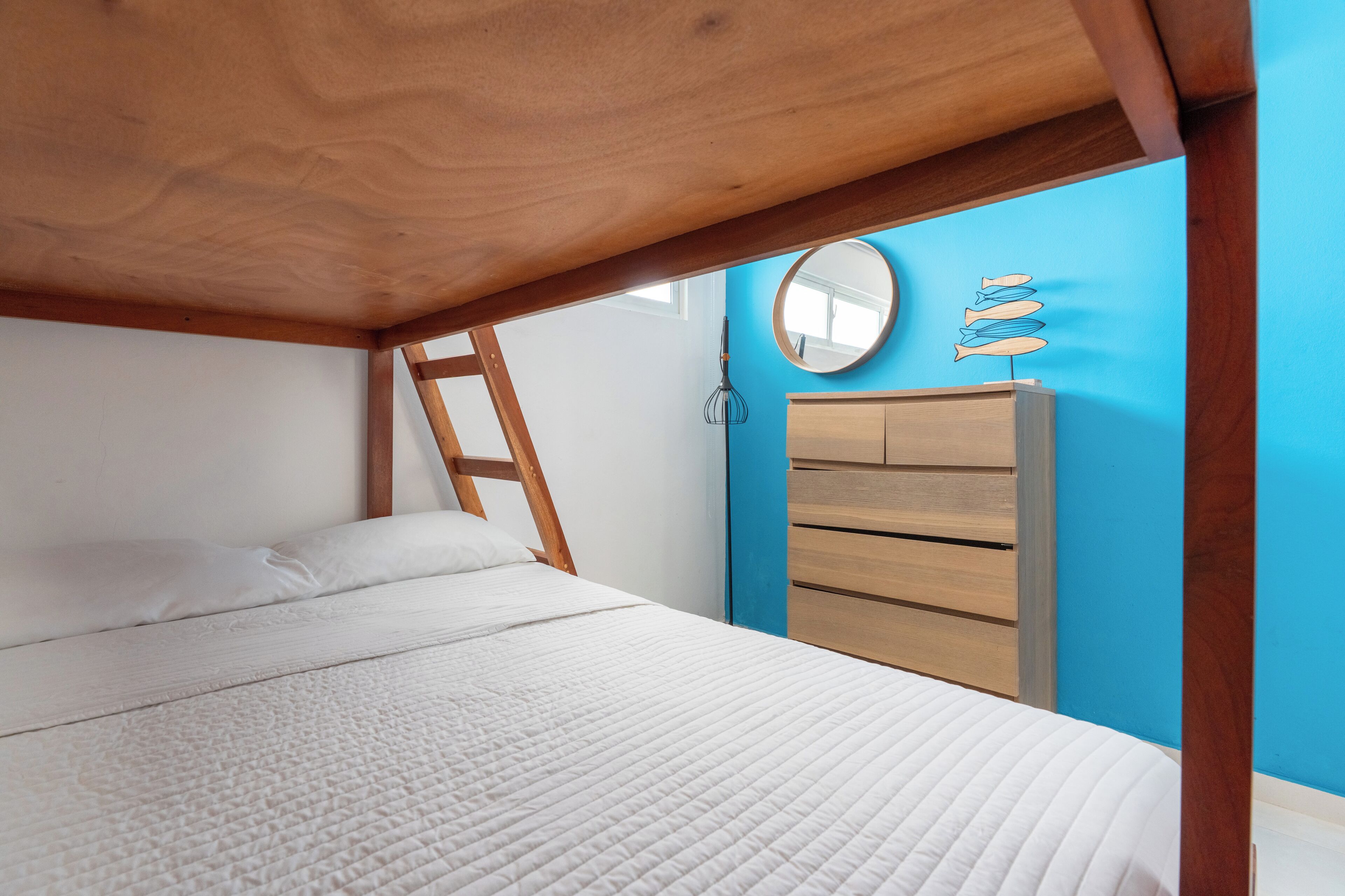 Un dormitorio con cabecera de cama de madera, colchón blanco, cómoda de madera y pared azul.