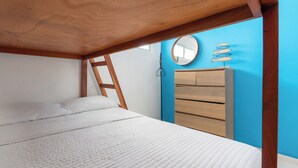 Un dormitorio con cabecera de cama de madera, colchón blanco, cómoda de madera y pared azul.