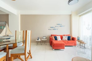 A modern living room with a glass dining table, a sofa, and a wall art piece. - Azul | Pool View, 5-Minute Walk to the Beach (Playa Juan Dolio)