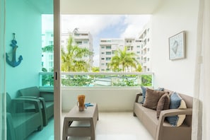 A balcony with wicker furniture, a view of a building, and a framed poster. - Azul | Pool View, 5-Minute Walk to the Beach (Playa Juan Dolio)