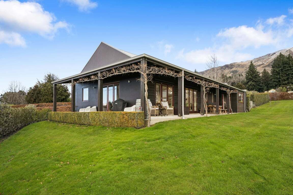 A modern house with a covered patio, a stone wall, and a grassy lawn.