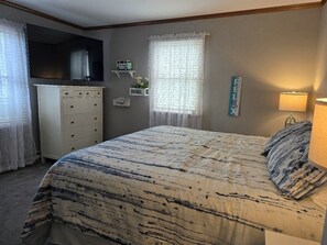 A bedroom with a bed, a dresser, a television, a window with curtains, and a wall decoration.