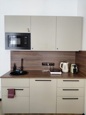 Eine Küchenzeile mit Mikrowelle, Kaffeemaschine, Wasserkocher, Spüle und einem Schrank mit Schubladen.