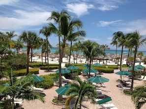 A resort with palm trees, lounge chairs, and umbrellas on a paved area with a view of the ocean. - Rare OCEANFRONT- Beautiful 2 Bed-Marriott Aruba Surf Club - Full Resort Access (Noord)