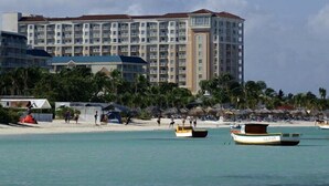 A hotel with multiple floors, a beach in the background, and several boats on the water. - OCEANFRONT- Beautiful 2 Bedroom-Marriott's Aruba Surf Club - Full Resort Access (Noord)