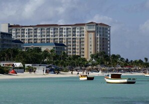 Un hotel de varios pisos, con una playa al fondo y varios barcos en el agua.