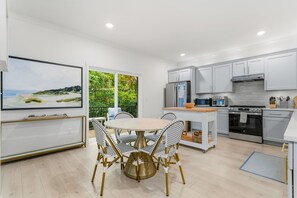 A modern kitchen with white cabinets, stainless steel appliances, and a dining area with a round table and wicker chairs. - South Haven Retreat • Indoor/Outdoor Pool • Beach (South Haven)