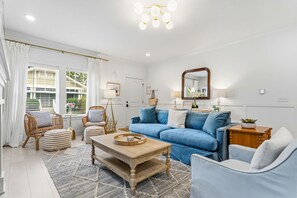 A modern living room with a blue sofa, a wooden coffee table, wicker chairs, and a large mirror. - South Haven Retreat • Indoor/Outdoor Pool • Beach (South Haven)