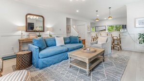A modern living room with a blue sofa, a coffee table, and a dining area with chairs. - South Haven Retreat • Indoor/Outdoor Pool • Beach (South Haven)