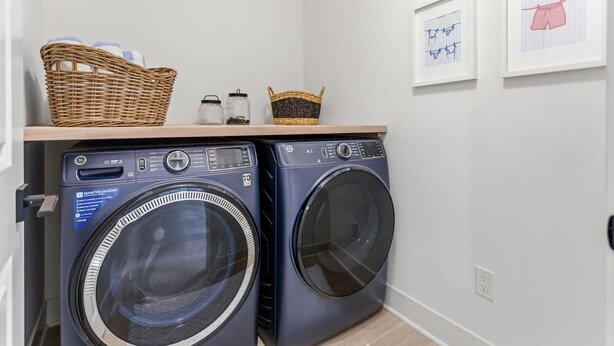 A laundry area with two front-loading washing machines, a shelf with baskets, and framed pictures on the wall. - South Haven Retreat • Indoor/Outdoor Pool • Beach (South Haven)