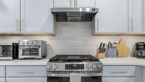 A kitchen with white cabinets, a stainless steel range, a microwave, and a coffee maker. - South Haven Retreat • Indoor/Outdoor Pool • Beach (South Haven)