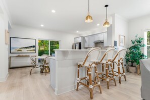 A modern kitchen with white cabinetry, a central island with bar stools, and pendant lighting. - South Haven Retreat • Indoor/Outdoor Pool • Beach (South Haven)