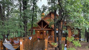 Une cabane en bois avec un porche, entourée d’arbres et d’un jardin.