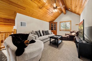 A cozy living room with a high ceiling, a fireplace, a sofa, a coffee table, a television, and a dog. - Trade the Heat for the Pines: Pinetop Family Cabin, Kayaks & Cool Nights (Pinetop)