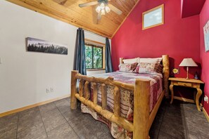 A bedroom with a wooden bed frame, a window with curtains, a ceiling fan, and a red wall. - Trade the Heat for the Pines: Pinetop Family Cabin, Kayaks & Cool Nights (Pinetop)