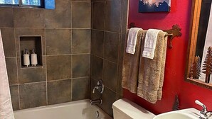 Une salle de bain équipée d’une baignoire, de toilettes et d’un lavabo, avec des carreaux de pierre et un mur rouge.