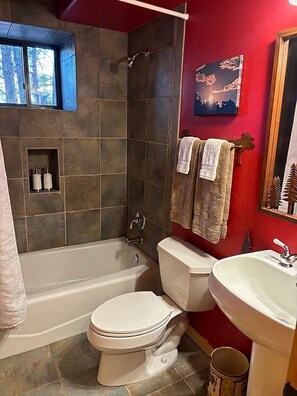 Ein Badezimmer mit Badewanne, Toilette und Waschbecken, mit Steinfliesen und einer roten Wand.