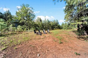 An outdoor area with a dirt ground, surrounded by trees and a wooden structure with Adirondack chairs. - Trade the Heat for the Pines: Pinetop Family Cabin, Kayaks & Cool Nights (Pinetop)