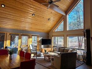 A spacious living area with a high ceiling, large windows, and a fireplace.