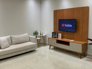 A modern living room with a sofa, a small round table with a plant, a decorative item, and a TV mounted on a wooden wall. - Vista Imperial Diamantina - Comfort and Nature in Harmony. (Diamantina)