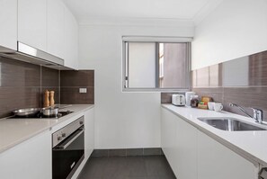 Eine kleine Küche mit Herd, Backofen, Spüle und einem Fenster über der Arbeitsfläche.