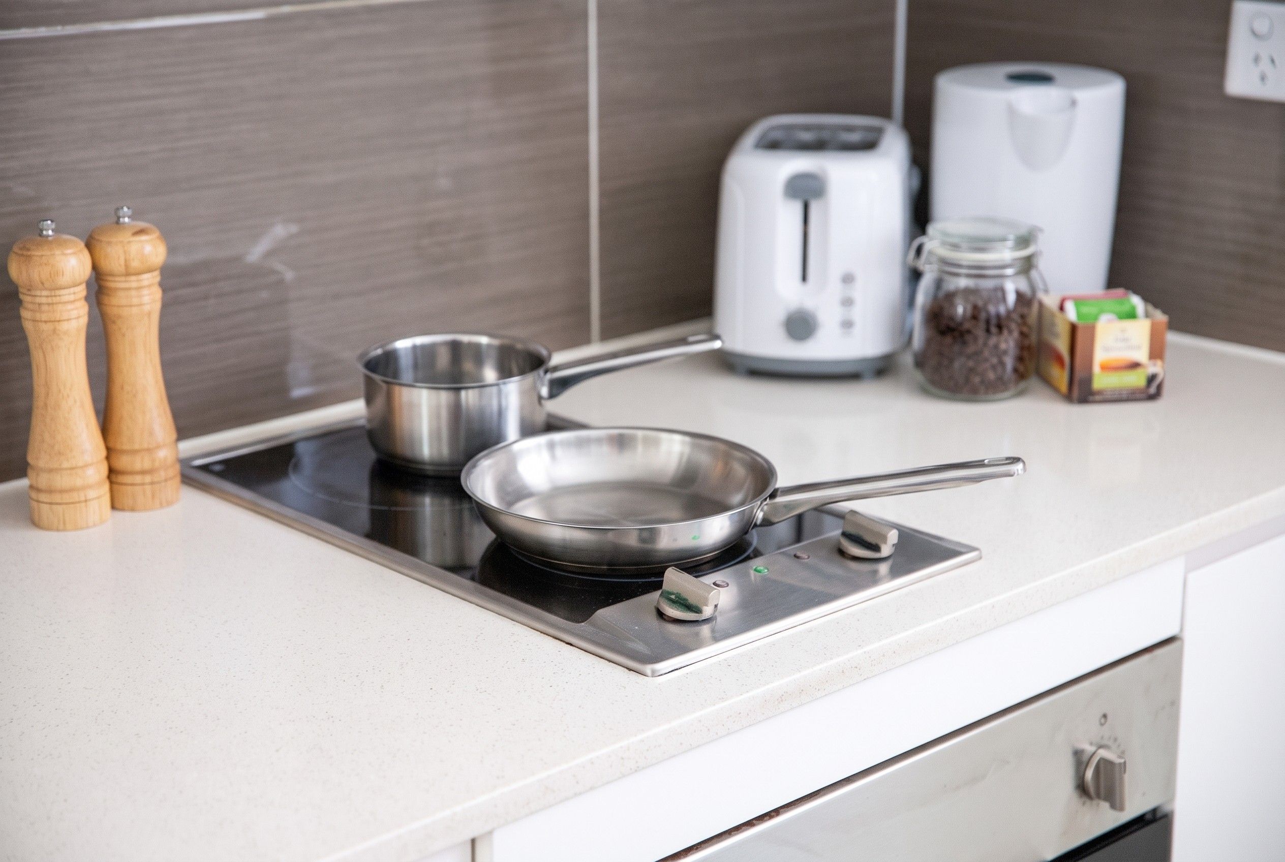 A kitchen with a stovetop, a frying pan, a pot, a toaster, and a jar of spices.