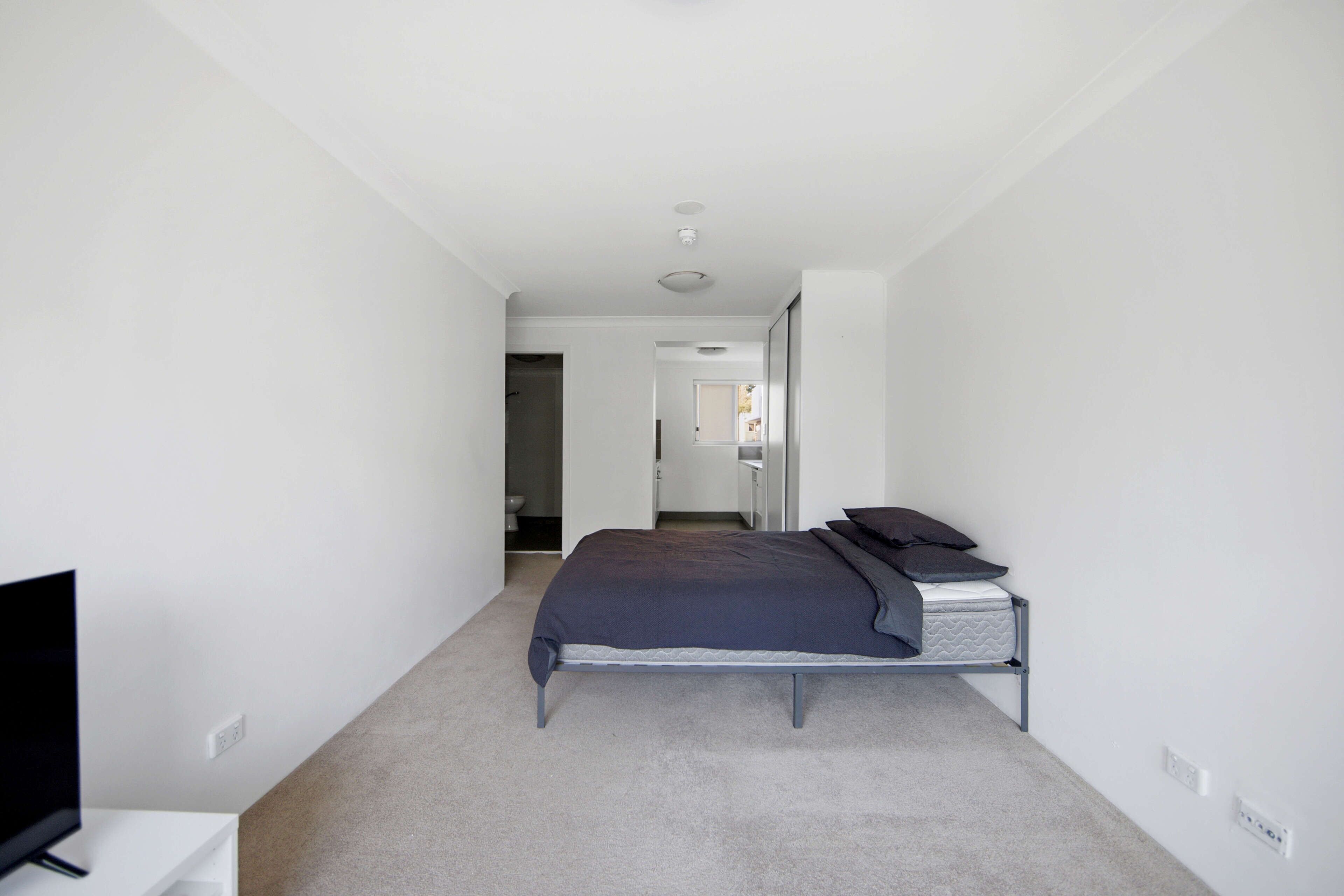 Une chambre à coucher avec un lit, une télévision et une salle de bain visible à travers une porte ouverte.