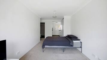 Une chambre à coucher avec un lit, une télévision et une salle de bain visible à travers une porte ouverte.