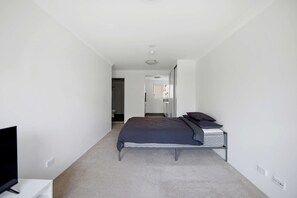A bedroom with a bed, a television, and a bathroom visible through an open door. - Bondi Beach Studio | Private Balcony & Kitchen (Bondi Beach)