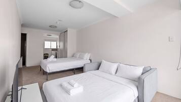 Une chambre d’hôtel avec deux lits, un canapé, un bureau et une salle de bain visible au fond.