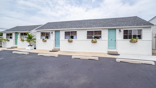A row of white motel buildings with teal doors and windows, each with a small planter. - Ocean Glass | Family Cottage | Pet-Friendly Stay | Steps to Sand (Rehoboth Beach)