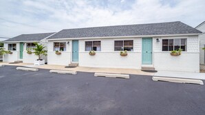 Un motel avec une rangée de chambres, chacune dotée d’une porte, de fenêtres et de plantes en pot.