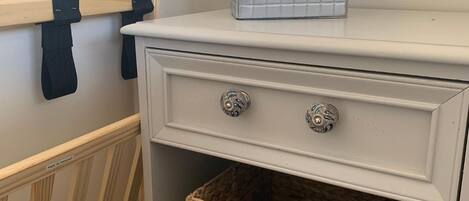 A white dresser with two drawers and a woven basket on the lower shelf.